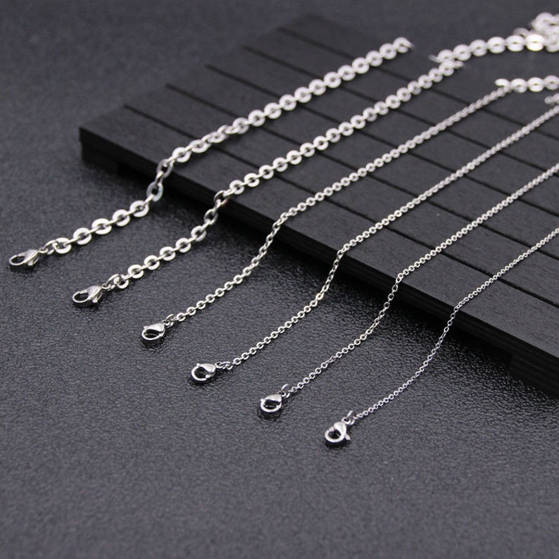 May include: Five silver chains of varying lengths, each with a lobster clasp closure. The chains are arranged in order of length, with the shortest chain at the top and the longest chain at the bottom.