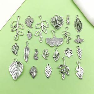 Könnte beinhalten: Eine Sammlung von 20 silberfarbenen Metall-Blätter-Anhängern mit verschiedenen Blattformen und -designs, darunter Zweige, Ginkgoblätter und einfache Blattskizzen.