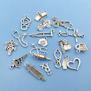May include: A collection of silver-toned metal charms with medical themes, including a stethoscope, a heart rate monitor, a syringe, a pill bottle, a crutch, an ambulance, and a nurse's cap. The charms are perfect for jewelry making or scrapbooking.