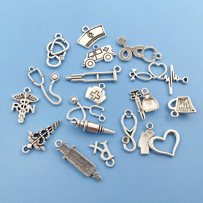 May include: A collection of silver-toned metal charms with medical themes, including a stethoscope, a heart rate monitor, a syringe, a pill bottle, a crutch, an ambulance, and a nurse's cap. The charms are perfect for jewelry making or scrapbooking.