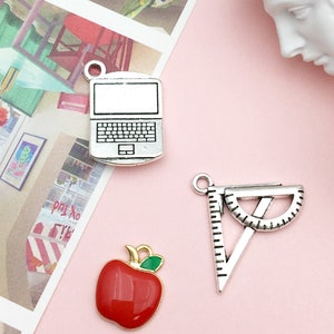 May include: Three silver charms with enamel accents. The charms are a red apple, a laptop computer, and a protractor.