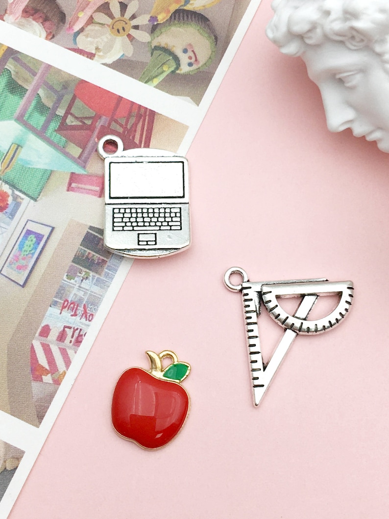 May include: Three silver charms with enamel accents. The charms are a red apple, a laptop computer, and a protractor.