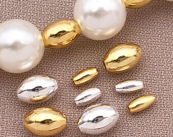 May include: A collection of gold and silver oval beads. The beads are of varying sizes and are arranged in a row on a textured surface.