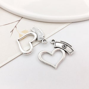 May include: Two silver charm pendants, each featuring a heart-shaped frame with a nurse's cap on top. The caps have a cross design.