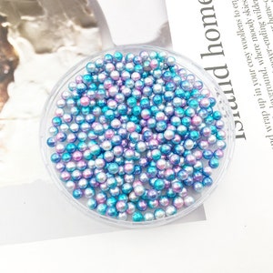 May include: A clear plastic container filled with iridescent blue and pink pearl beads.