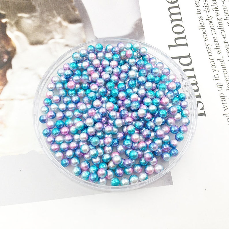 May include: A clear plastic container filled with iridescent blue and pink pearl beads.