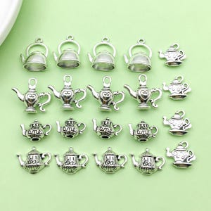 May include: A collection of 18 silver-toned teapot charms with various designs, including hearts, teapots, and the words "tea time".