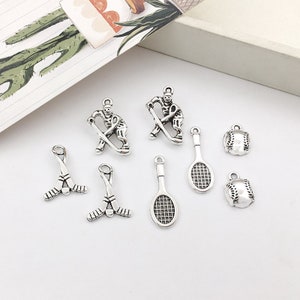 以下が含まれることがあります： スポーツをテーマにした銀色の金属製チャームのセット。チャームには、ホッケー選手、野球、テニスラケット、ホッケースティックが含まれています。