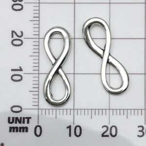 May include: Two silver infinity symbol charms, each measuring approximately 1.5 cm in length, are displayed against a white grid background.