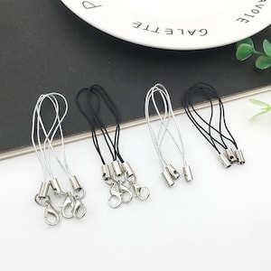 Op de afbeelding: Zes zilveren sleutelhangers met zwarte en zilveren koorden. De sleutelhangers hebben een zilveren lus en een zilveren tonvormige sluiting.