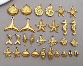 May include: A collection of gold-colored charms in various sea-themed shapes, including seashells, starfish, seahorses, fish, and turtles. Each charm has a small loop for attaching to jewelry or other crafts. The charms are arranged on a light gray surface.