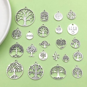 Puede incluir: Una colección de 19 dijes de metal plateados con diseños de árbol de la vida. Los dijes son de varias formas, incluyendo círculos, corazones y rectángulos. Algunos dijes tienen detalles adicionales, como las palabras "Life is a Gift" y "My Family My Love".
