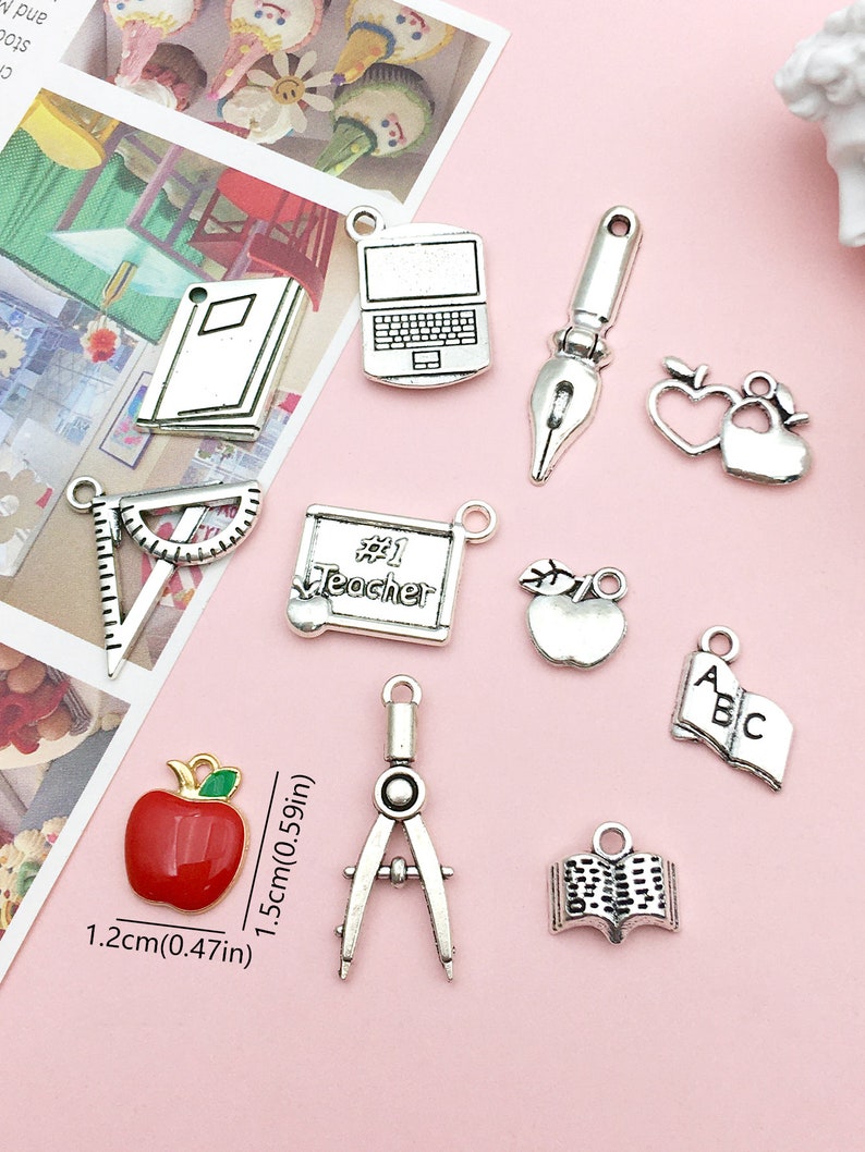 May include: A set of 10 silver charm pendants with school-themed designs, including an apple, a book, a laptop, a compass, a ruler, a paintbrush, a heart, and a chalkboard with the text "#1 Teacher".