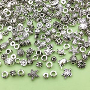 May include: A collection of silver-toned metal beads featuring a variety of sea-themed designs, such as fish, seashells, starfish, and seahorses. The beads are ideal for jewellery making or crafting.