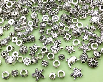 May include: A collection of silver-toned metal beads featuring a variety of sea-themed designs, such as fish, seashells, starfish, and seahorses. The beads are ideal for jewellery making or crafting.