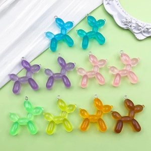 Può includere: Una collezione di ciondoli a forma di cane traslucidi e colorati. I ciondoli sono in vari colori, tra cui blu, viola, rosa, verde, giallo, arancione e marrone. Ogni ciondolo ha un piccolo anello argentato nella parte superiore per il fissaggio.