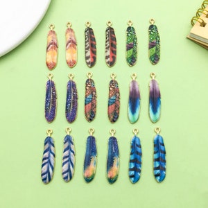 Könnte beinhalten: Sortiment von 18 goldfarbenen Federschmuckstücken mit bunten bedruckten Designs. Die Charms sind perfekt für die Schmuckherstellung, das Scrapbooking und andere Bastelprojekte.
