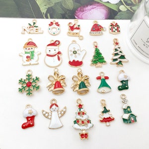 May include: Assortment of 20 gold-tone Christmas charm pendants with enamel details. Charms include a snowman, a Christmas tree, a snowflake, a stocking, a bell, a mitten, an angel, a house, and a "Noel" sign.