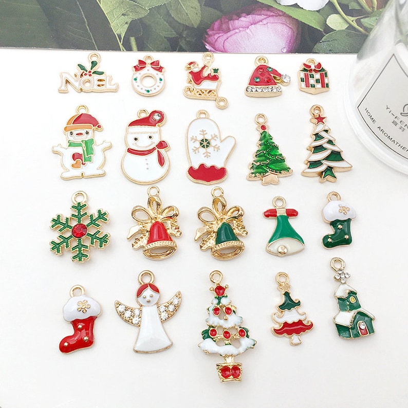 May include: Assortment of 20 gold-tone Christmas charm pendants with enamel details. Charms include a snowman, a Christmas tree, a snowflake, a stocking, a bell, a mitten, an angel, a house, and a "Noel" sign.