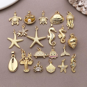 Puede incluir: Una colección de dijes de metal en tono dorado con varios diseños de vida marina, incluyendo tortugas, estrellas de mar, caballitos de mar, conchas, una langosta, un cangrejo y una medusa. Algunos dijes tienen cristales y una perla.