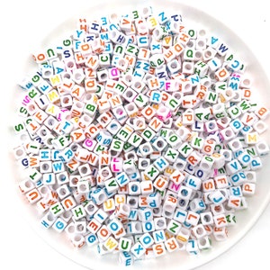 May include: A large pile of white plastic letter beads with colorful letters. The beads are in a variety of colors, including red, blue, green, yellow, and orange.