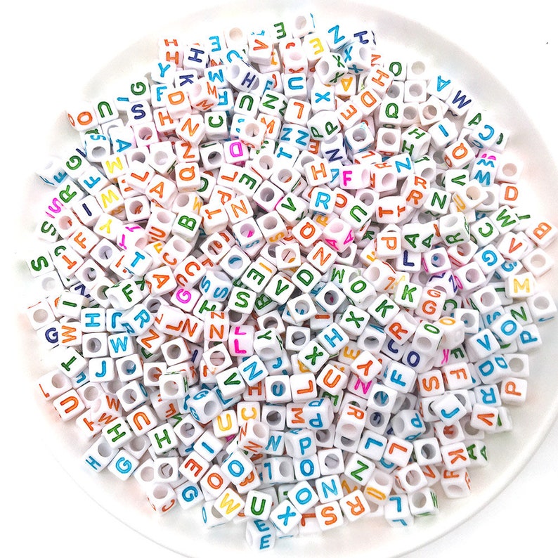 May include: A large pile of white plastic letter beads with colorful letters. The beads are in a variety of colors, including red, blue, green, yellow, and orange.