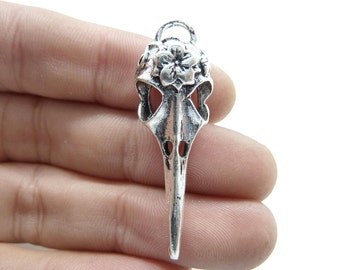 May include: Silver pendant featuring a detailed bird skull with floral accents. The skull has a long, pointed beak and intricate details.