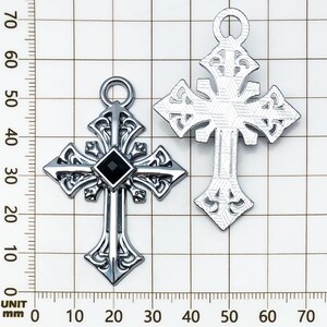 May include: Two silver-colored crosses. One cross features a black square gem at the center. Both crosses have ornate, gothic-style designs with a loop at the top for hanging. The crosses are displayed against a grid background.