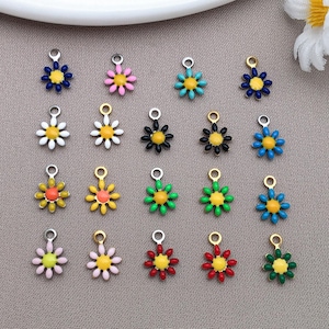 May include: A collection of daisy-shaped charms in various colors, including blue, pink, yellow, black, green, and red. Each charm has a yellow center and a silver or gold-colored loop for attaching to jewelry or crafts. The charms are arranged on a neutral background.