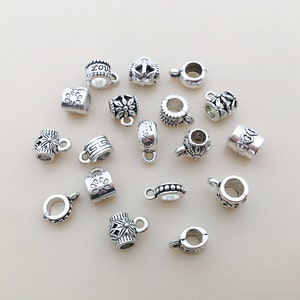 Puede incluir: Una colección de tapas de cuentas de metal plateadas con varios diseños, incluyendo florales, geométricos y de escritura. Las tapas de cuentas tienen un agujero para enhebrar y un bucle para sujetar a las joyas.