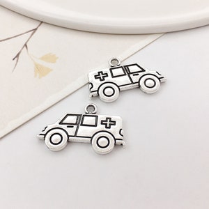 May include: Two silver-toned metal charms shaped like ambulances. Each charm has a black outline and a black cross on the side.