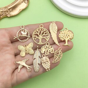 May include: A set of ten gold-toned metal charms featuring various nature-inspired designs, including a tree, an owl, a butterfly, a feather, a leaf, an elephant, a bird, and a pair of wings.