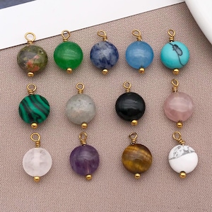 May include: A collection of twelve gemstone pendants with gold-colored metal loops. The pendants are round and feature various colors and patterns, including green, blue, black, pink, and brown. Each pendant has a small gold bead at the bottom.