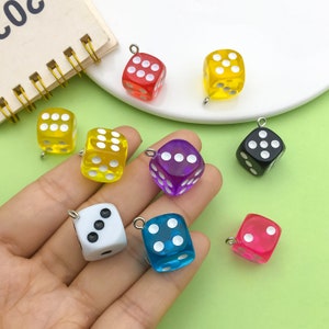May include: Assortment of colorful dice charms with silver loops. The dice are made of clear plastic and have white dots. The colors include red, yellow, purple, blue, black, and pink.