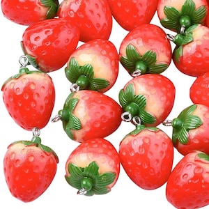 May include: A collection of red and green strawberry-shaped charms with silver loops. The charms are made of plastic and have a glossy finish.