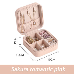May include: A pink faux leather jewelry box with a zipper closure. The box has six compartments for storing earrings, rings, and necklaces. The box measures 10 inches by 10 inches by 5 inches.