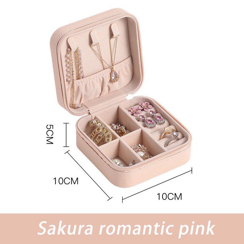 May include: A pink faux leather jewelry box with a zipper closure. The box has six compartments for storing earrings, rings, and necklaces. The box measures 10 inches by 10 inches by 5 inches.