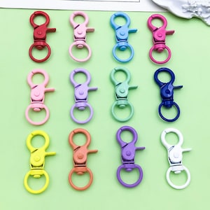 May include: A collection of colorful swivel snap hooks in various shades, including red, pink, blue, green, yellow, orange, purple, and white. These metal clasps are designed for keychains, lanyards, or crafting projects.