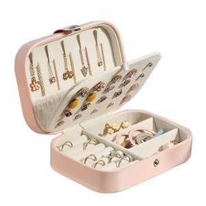 May include: A pink faux leather jewellery box with a hinged lid. The box has multiple compartments for storing earrings, rings, and other jewellery. The box is open and the compartments are filled with various jewellery.