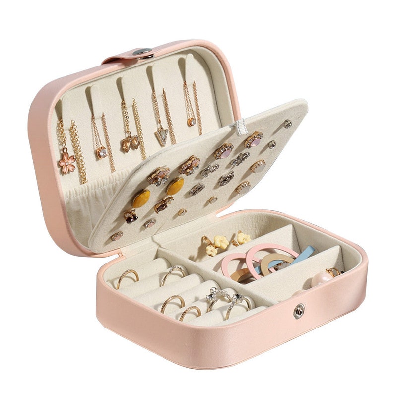 May include: A pink faux leather jewellery box with a hinged lid. The box has multiple compartments for storing earrings, rings, and other jewellery. The box is open and the compartments are filled with various jewellery.