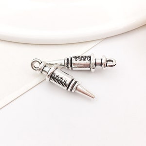 May include: Two silver-toned metal syringe charms with black markings. The charms are in the shape of a syringe with a needle and a plunger. The markings on the syringes read "4321" and "4321".