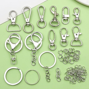 Puede incluir: Una colección de llaveros y anillos para llaves de color plateado sobre una superficie verde claro. El surtido incluye varios estilos de cierres, anillas y cadenas de conexión, adecuados para manualidades u organización de llaves.