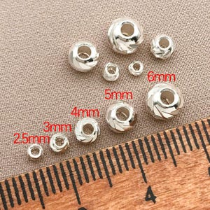 May include: An assortment of silver beads in different sizes, from 2.5mm to 6mm. Some beads feature a spiral pattern. Sizes are indicated in red text. A wooden ruler is in the foreground.