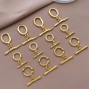 May include: A set of ten gold-toned metal toggle clasps. Each clasp features a round loop and a straight bar with a rounded end.