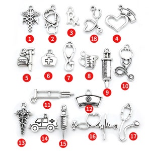 May include: A set of 17 silver-toned metal charms with various medical and nursing themes. The charms include a stethoscope, a heart, a syringe, a pill bottle, a nurse's hat, a medical symbol, a measuring cup, a crutch, an ambulance, and more.