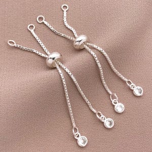 K&ouml;nnte beinhalten: Zwei verstellbare Armb&auml;nder aus Silber mit klaren Kristall-Akzenten. Jede Kette hat eine kleine runde Perle und eine verschiebbare Perle zum Einstellen der L&auml;nge.