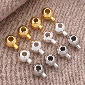 May include: A collection of 12 gold, silver, and black metal bead caps with a loop on one end. The bead caps are arranged in three rows of four.