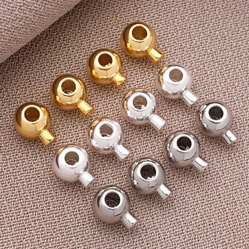 May include: A collection of 12 gold, silver, and black metal bead caps with a loop on one end. The bead caps are arranged in three rows of four.
