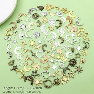 Könnte beinhalten: Eine Sammlung von Charms mit Himmelsmotiven in verschiedenen Metallausführungen, darunter Gold, Silber und Bronze. Die Charms zeigen Monde, Sterne und Sonnen und sind 1-2 cm lang. Sie liegen auf einem hellgrünen Hintergrund.