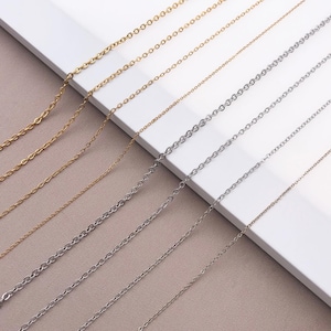 Könnte beinhalten: Eine Auswahl an filigranen Kettenhalsketten in Gold- und Silberfarben. Die Ketten, in verschiedenen Stärken und Gliederarten, sind auf neutralem Hintergrund angeordnet. Ideal für Schmuckherstellung oder zum Kombinieren.